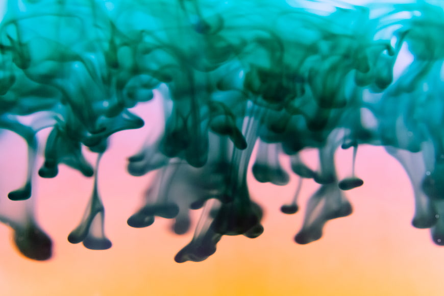 Abstract teal ink swirling in water with pink and orange gradient background