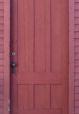 Close-up of a rustic red wooden barn door with vintage hardware