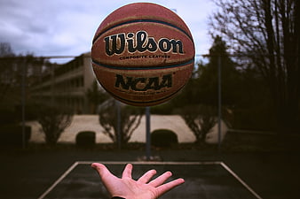Wilson NCAA Basketball in Mid-Air Above Hand on Court