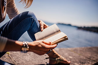Woman Reading Book by the Sea on Sunny Day