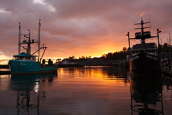 Fishing boats docked in harbor at sunset with colorful sky