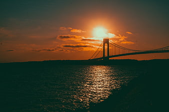 Silhouette of suspension bridge at sunset over water