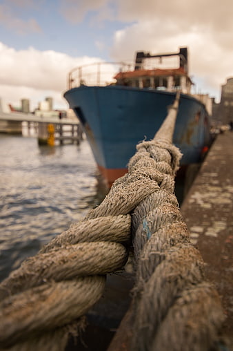 Close-up of weathered rope knot on dock with blue boat