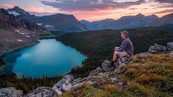 Hiker Sitting on Cliff Overlooking Turquoise Mountain Lake at Sunset