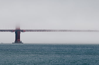 Red bridge tower emerging from thick fog over calm ocean water