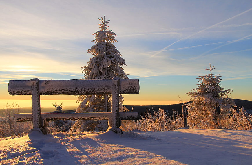 Snowy Wooden Bench on Mountain Peak at Sunset