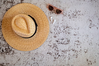 Summer vacation flat lay with straw hat, sunglasses, and wireless earbuds on textured background