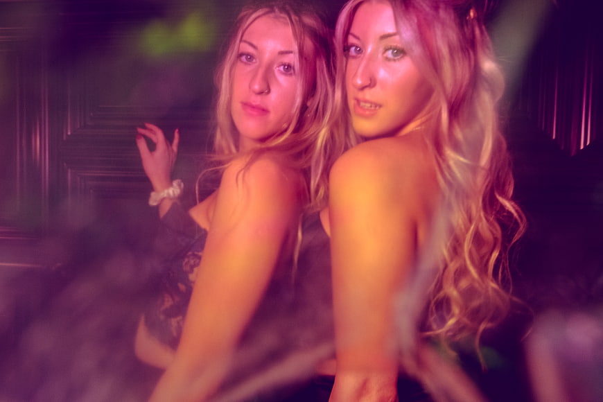 Two young women posing in a nightclub with purple lighting