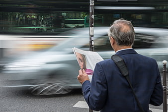 Senior man reading newspaper on busy city street with motion blur