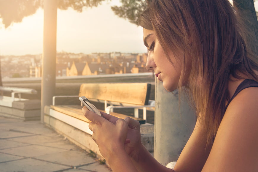 Young Woman Texting on Smartphone at Sunset