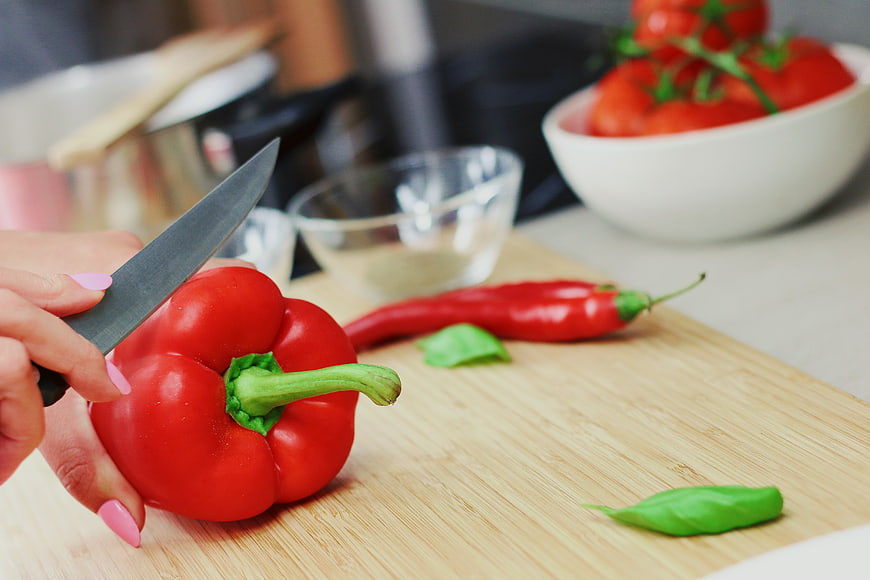 Woman cutting red bell pepper on wooden board