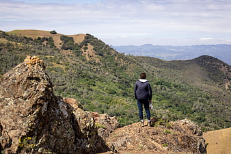 Hiker standing on rocky peak overlooking green mountain landscape