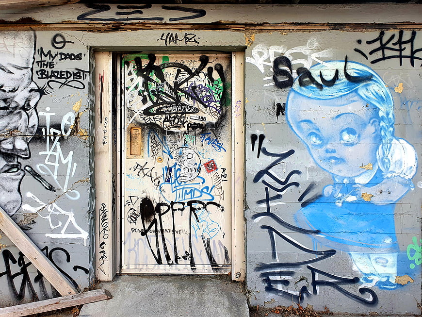 Urban graffiti mural with blue doll and tags on door