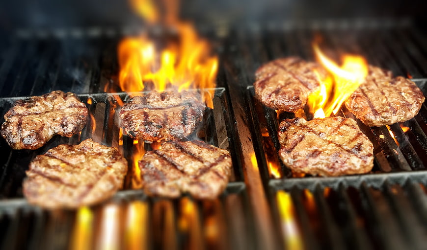 Juicy burger patties grilling with flames on barbecue