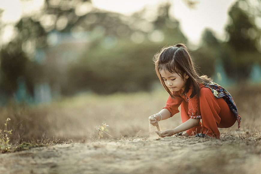 Little girl playing with sand in a field