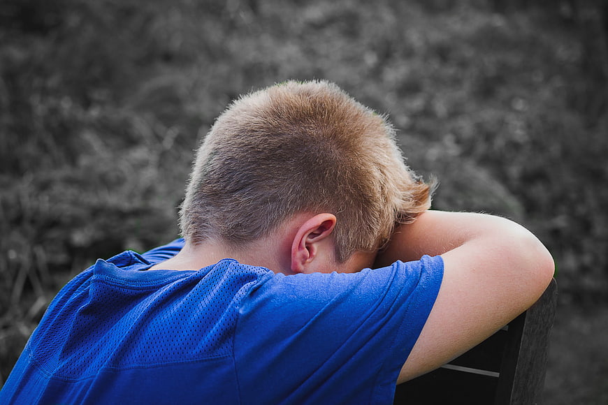 Sad Boy Resting Head on Arms in Blue Shirt