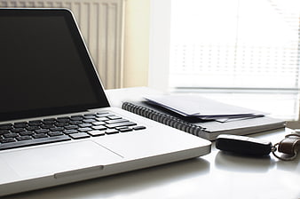 Laptop, car keys, and notebook on a white desk