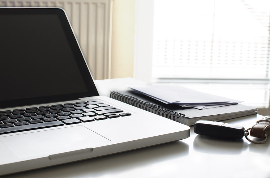 Laptop, car keys, and notebook on a white desk