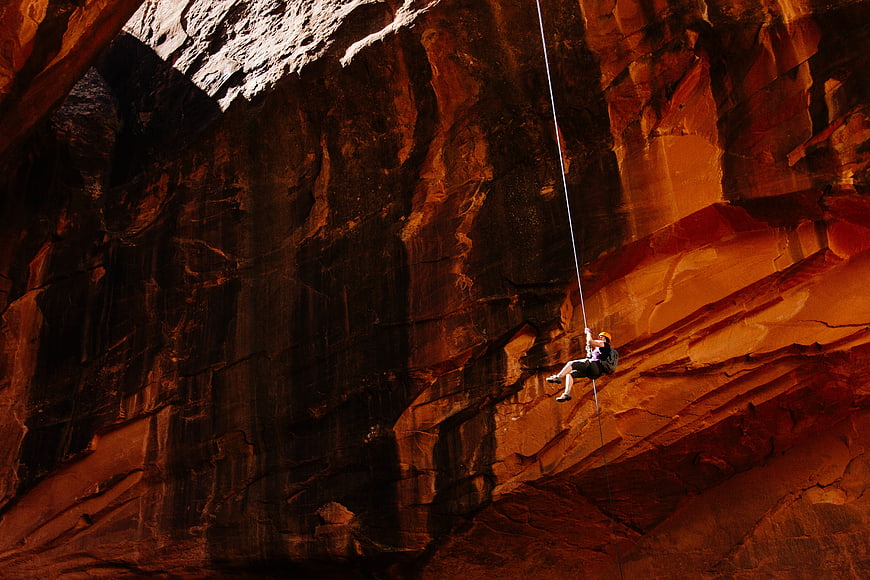 Woman rappelling down a massive red rock canyon wall