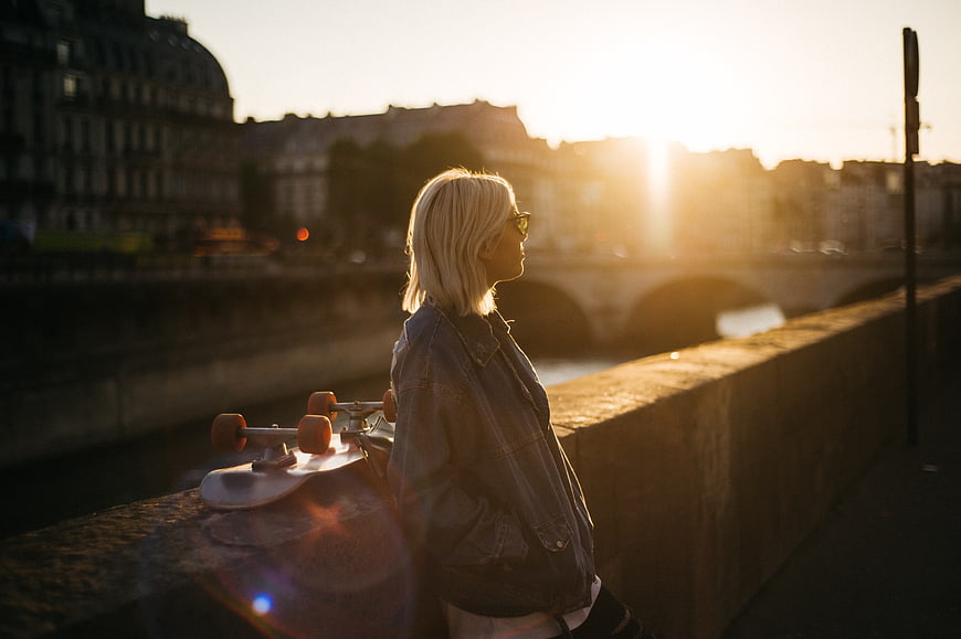 Woman with Skateboard on Bridge at Sunset
