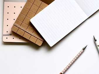 Flat lay of pink and brown notebooks with pens on white background