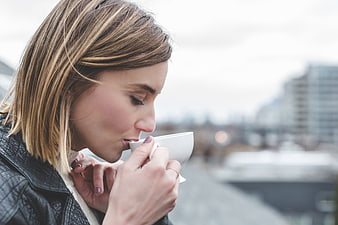Woman drinking coffee outdoors with blurred city background