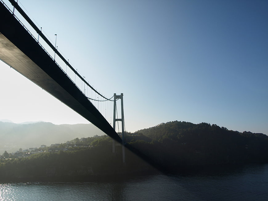 Silhouette of suspension bridge over misty water and hills