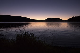 Serene Lake at Dusk with Silhouetted Hills and Reeds