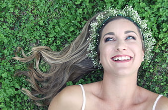 Happy woman with flower crown lying in clover field
