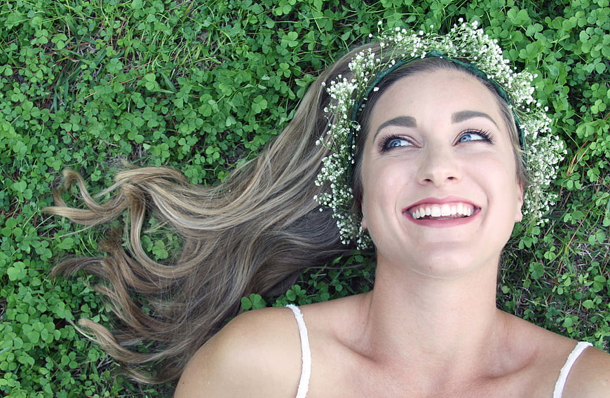 Happy woman with flower crown lying in clover field