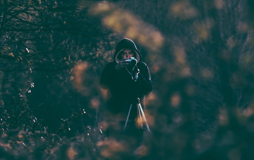 Mysterious hooded photographer in dark forest with camera