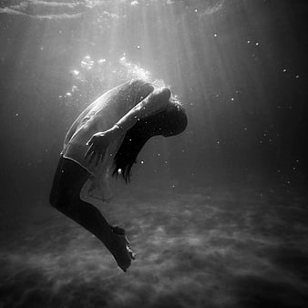 Woman diving underwater in black and white with light rays