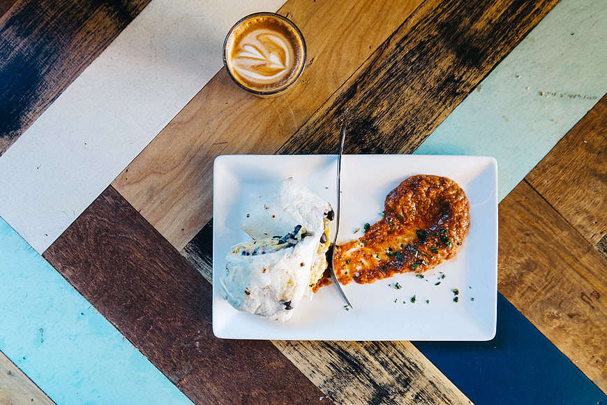 Overhead view of burrito and latte on colorful wooden table