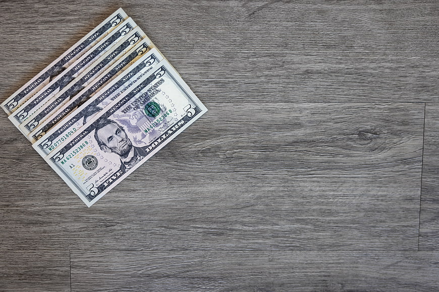 Stack of five dollar bills on gray wooden background