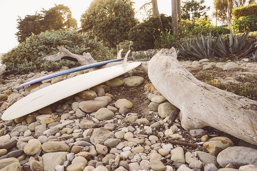 White surfboard resting on rocky beach with driftwood