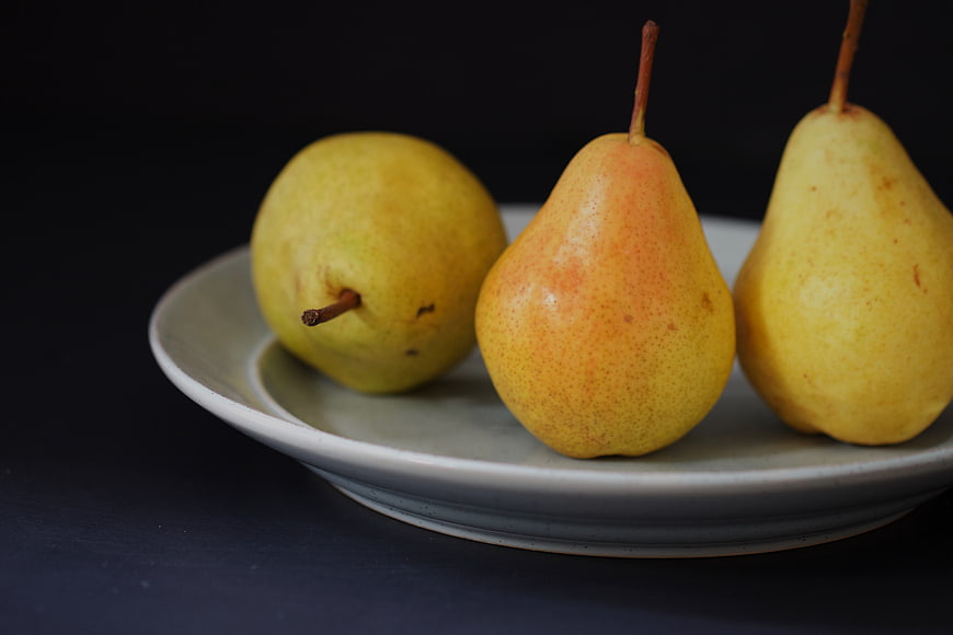 Three fresh yellow pears on a ceramic plate against dark background