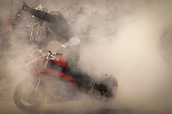 Motorcycle stunt rider performing burnout in thick smoke