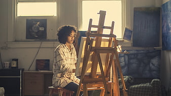 Young female artist painting in sunlit studio