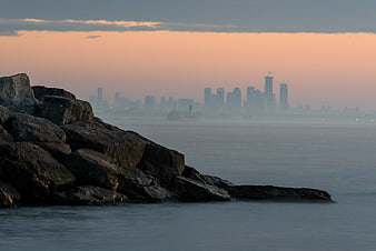 Distant City Skyline at Sunset Behind Rocky Shore