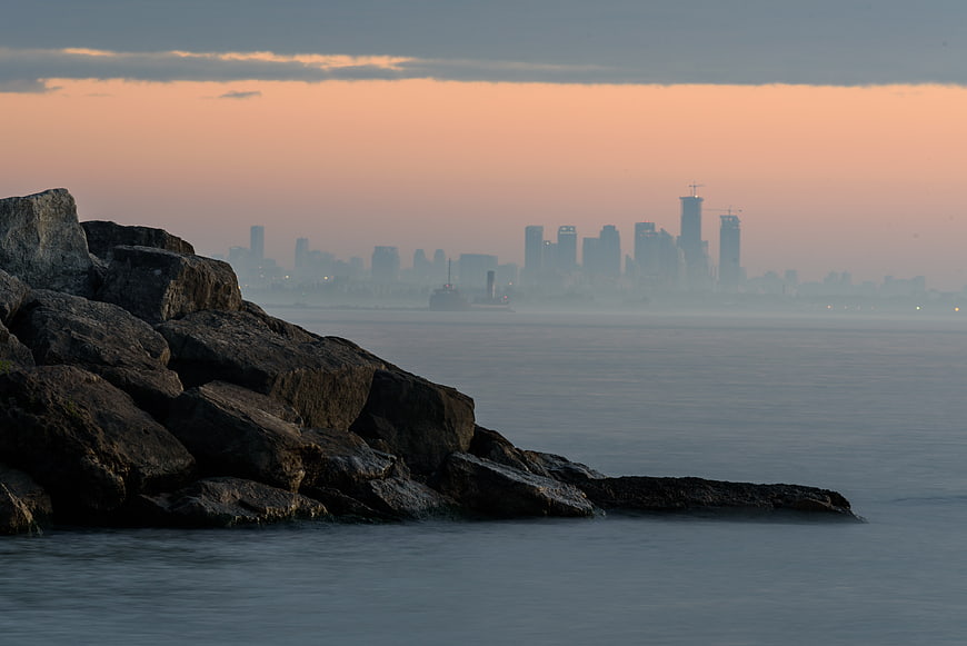 Distant City Skyline at Sunset Behind Rocky Shore