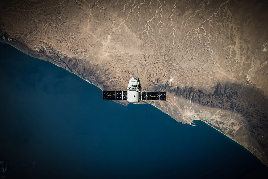Spacecraft orbiting Earth over desert coastline and ocean