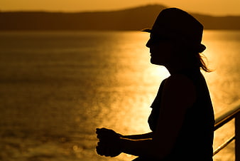 Silhouette of woman in hat watching golden sunset over ocean