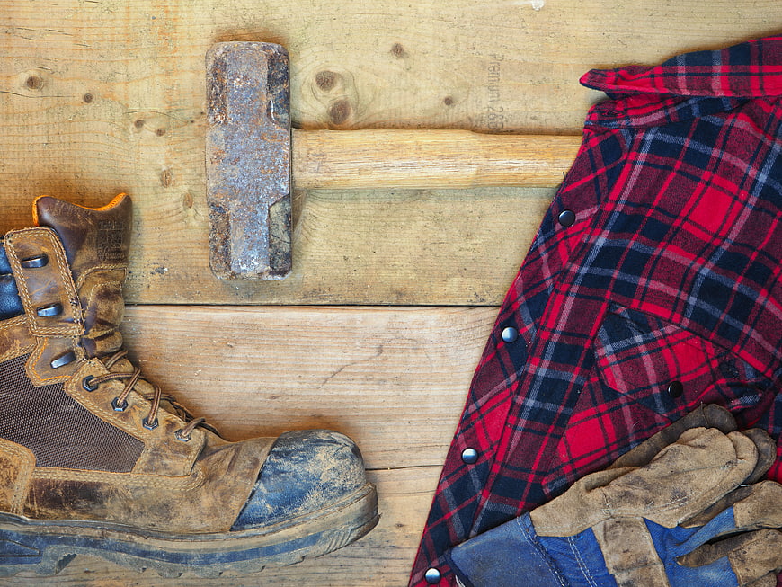 Work boots, sledgehammer, and plaid shirt on wooden background