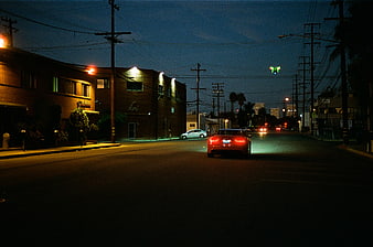 Red sports car driving down city street at night