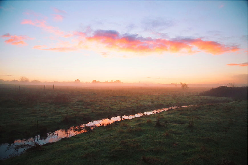 Misty Sunrise Over Rural Stream and Green Pasture