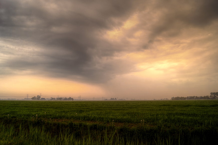 Dramatic Storm Clouds Over Green Rural Field at Sunset