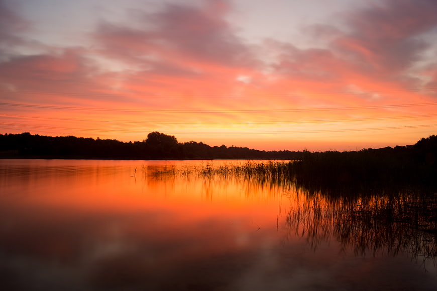 Vibrant Orange Sunset Reflection on Calm Lake with Silhouette