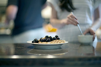 Waffles with blackberries on a kitchen counter with blurred couple