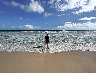 Man standing in ocean waves looking at horizon on sunny beach