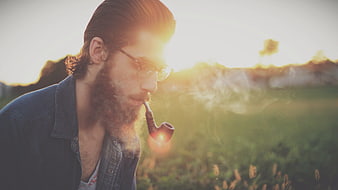 Bearded man smoking pipe in field at sunset